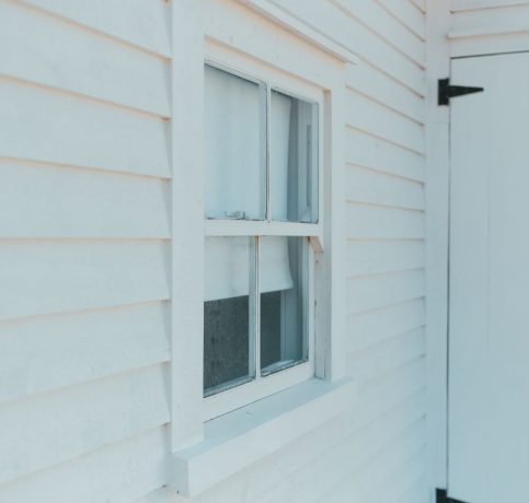 Close-up of a white wooden facade showcasing a window and door, highlighting minimalist architecture.